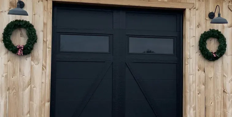 A white garage door with a pergola structure in front of a tan house with a tiled roof.