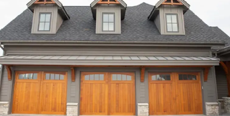 A dark grey, four-panel residential garage door with rectangular window inserts, set against a light stone exterior wall.