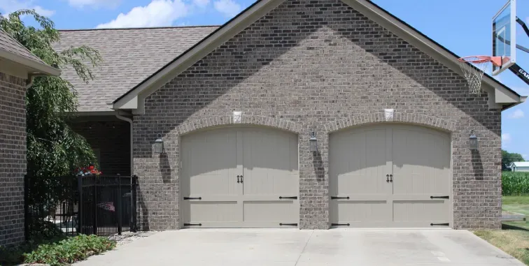 A white garage door with a pergola structure in front of a tan house with a tiled roof.