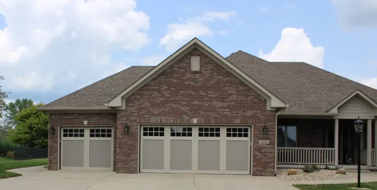 A modern home exterior with a light-colored garage door, a dark front door, stone walls, and a balcony with a black railing.