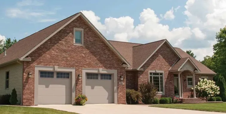 A white garage door with a pergola structure in front of a tan house with a tiled roof.