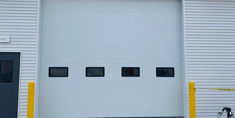 A white garage door with horizontal panels, framed by a decorative white wooden pergola, attached to a tan stucco house.