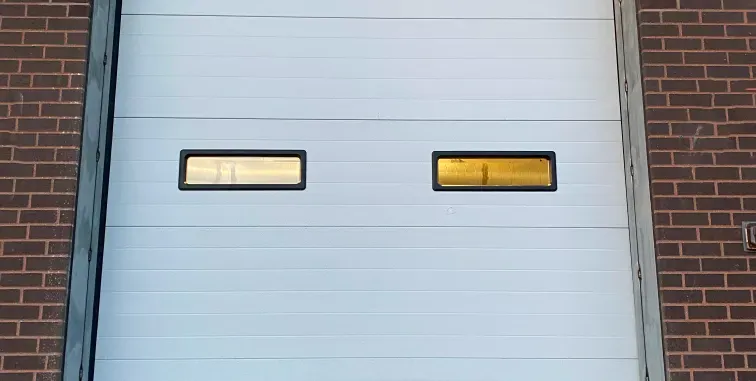 Three cream-colored carriage-style garage doors with arched stone trim on a brick house exterior.