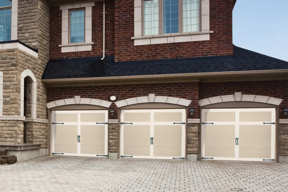 Three garage doors with carriage-style hardware on a stone-faced home with a paved driveway.