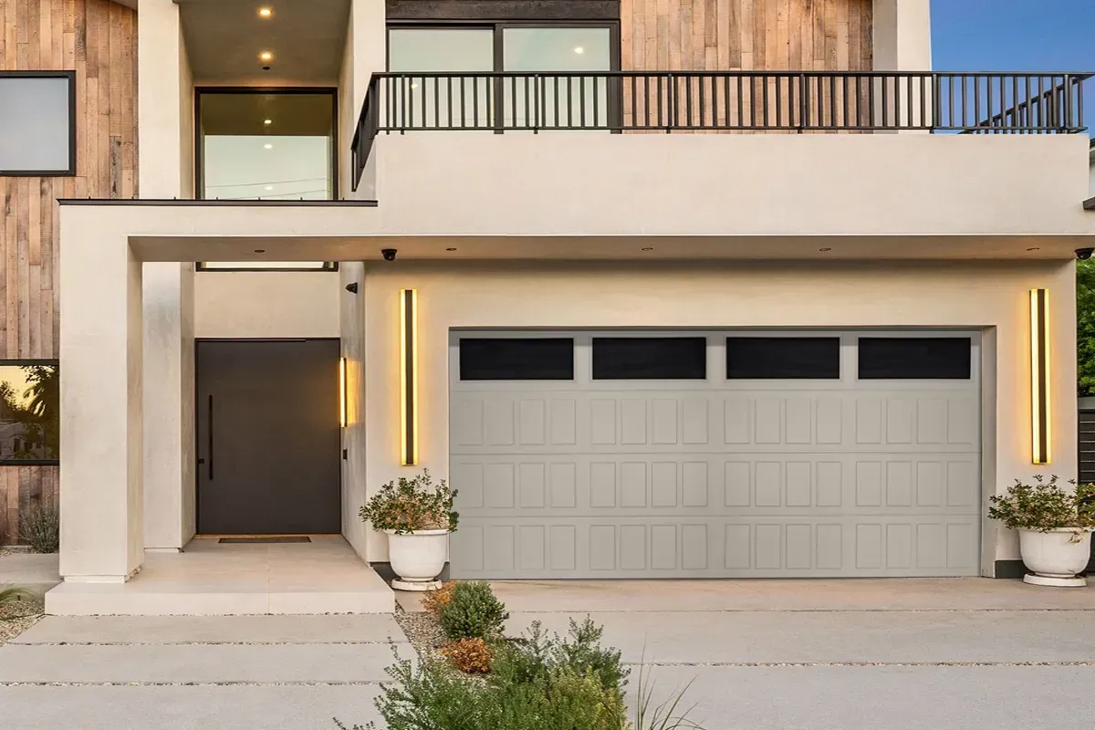 A modern home exterior with a light-colored garage door, a dark front door, stone walls, and a balcony with a black railing.