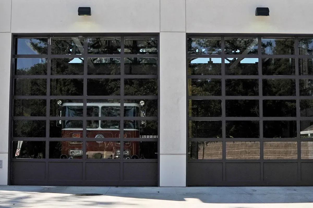 Two large, modern glass garage doors on a white building, with a fire truck visible through the left door.