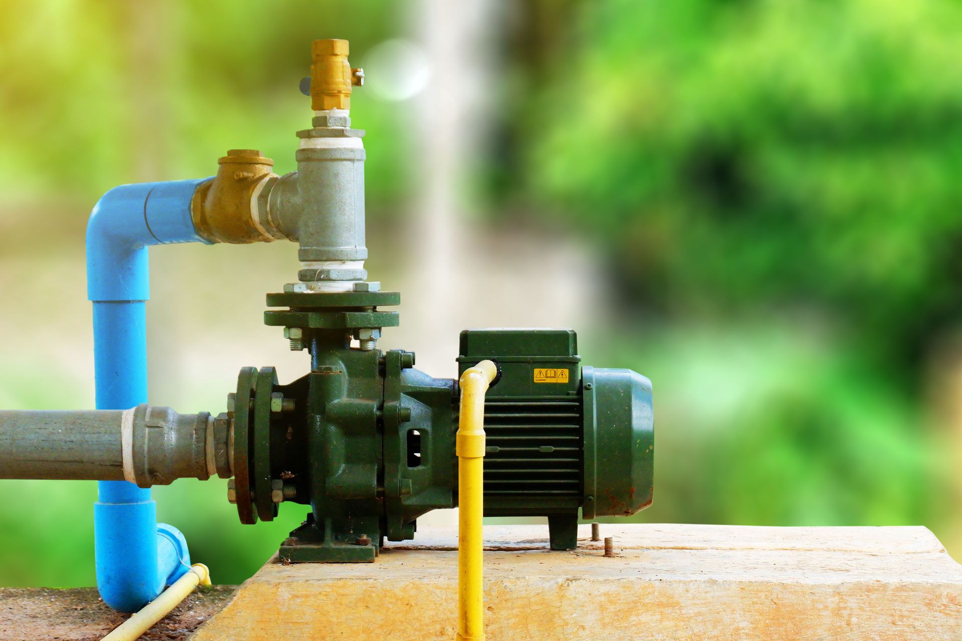 A big water pump motor for a water supply system with blurred foliage in the background.