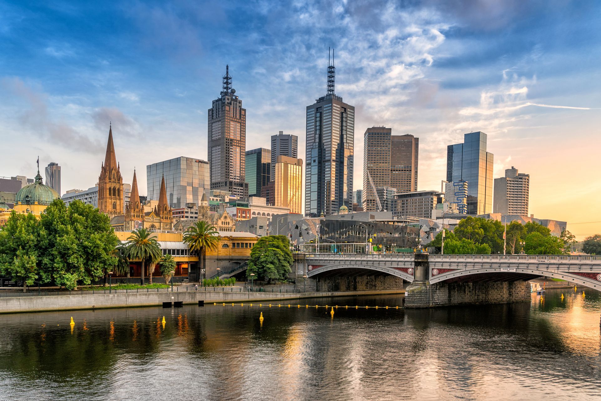 A city skyline with a river in the foreground and a bridge in the background.