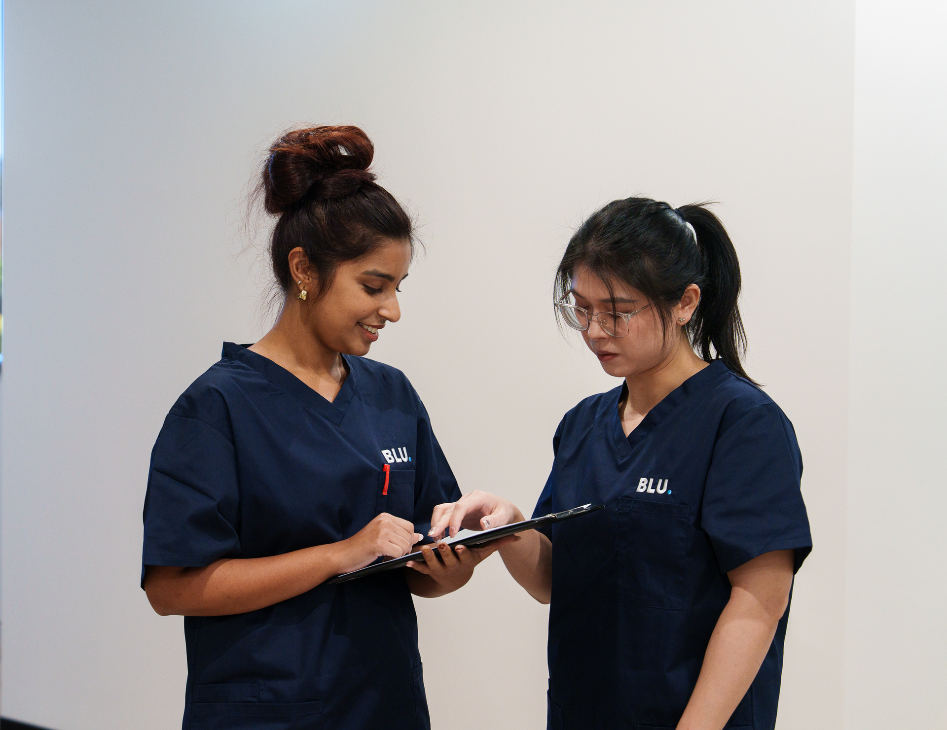 Two women in scrubs are looking at a clipboard.
