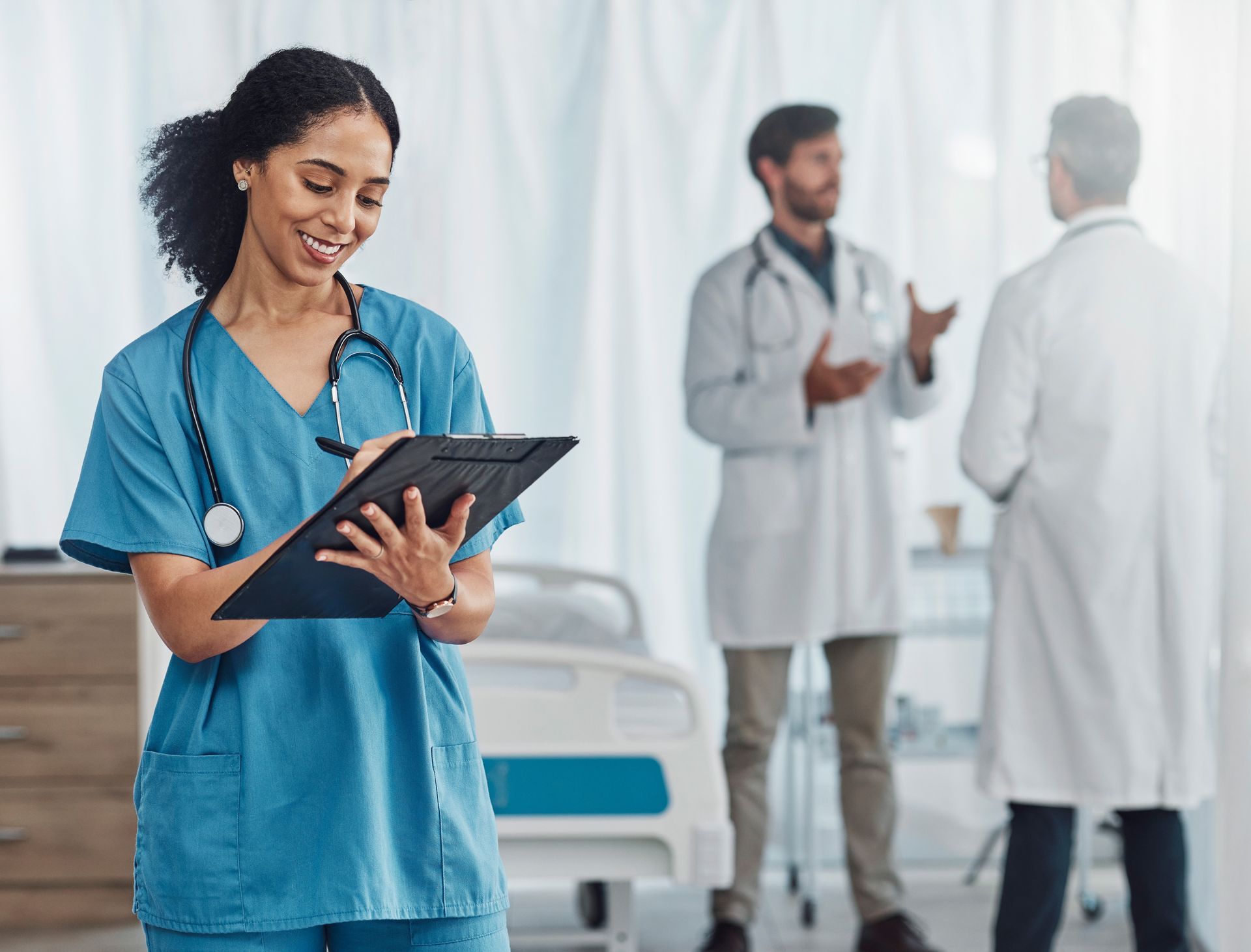A nurse is holding a clipboard in front of two doctors in a hospital room.