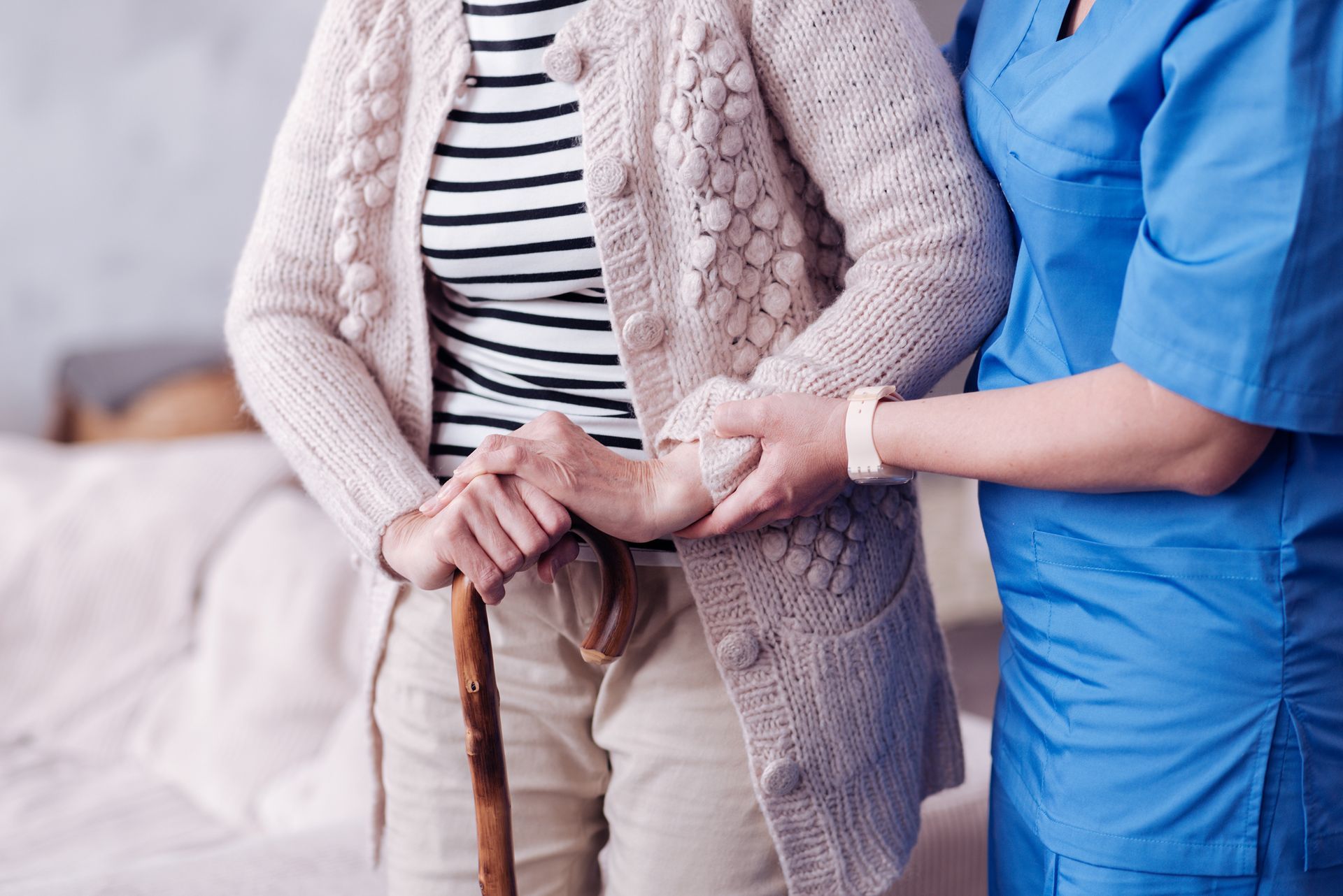 A nurse is helping an elderly woman with a cane.