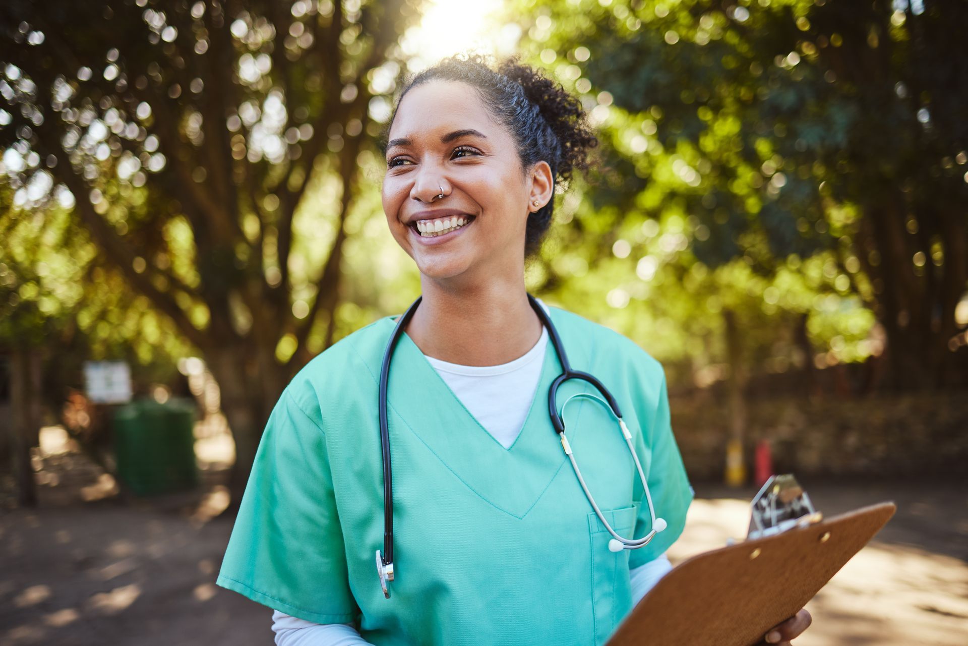 A nurse with a stethoscope around her neck is holding a clipboard and smiling.