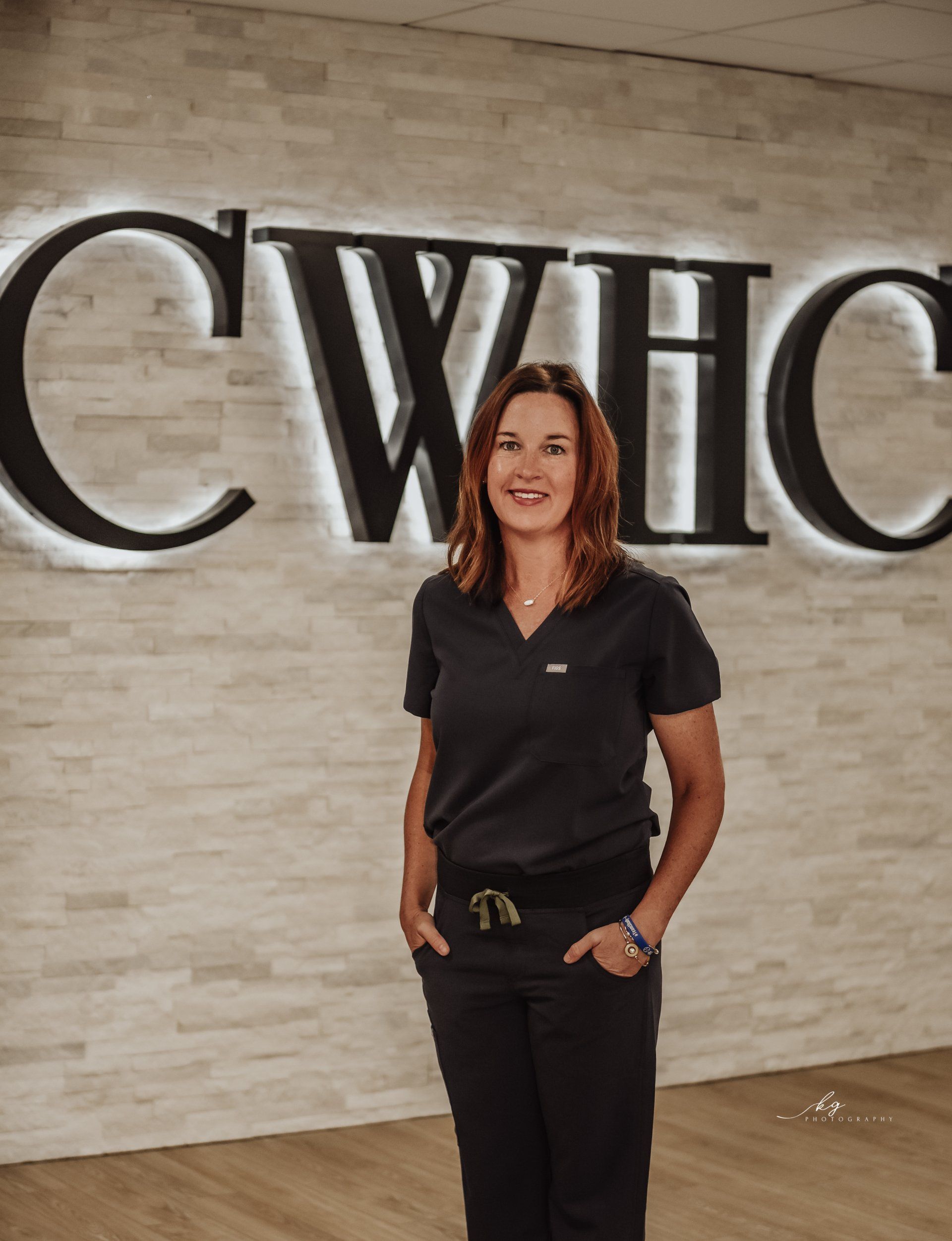 Professional wearing dark scrubs, standing in front of a wall with illuminated 