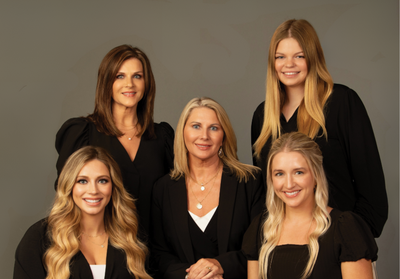 Five smiling people pose against a neutral grey background, wearing black business-casual attire.