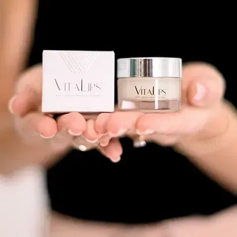 A pair of cupped hands holding a white box and a small glass jar, both labeled 