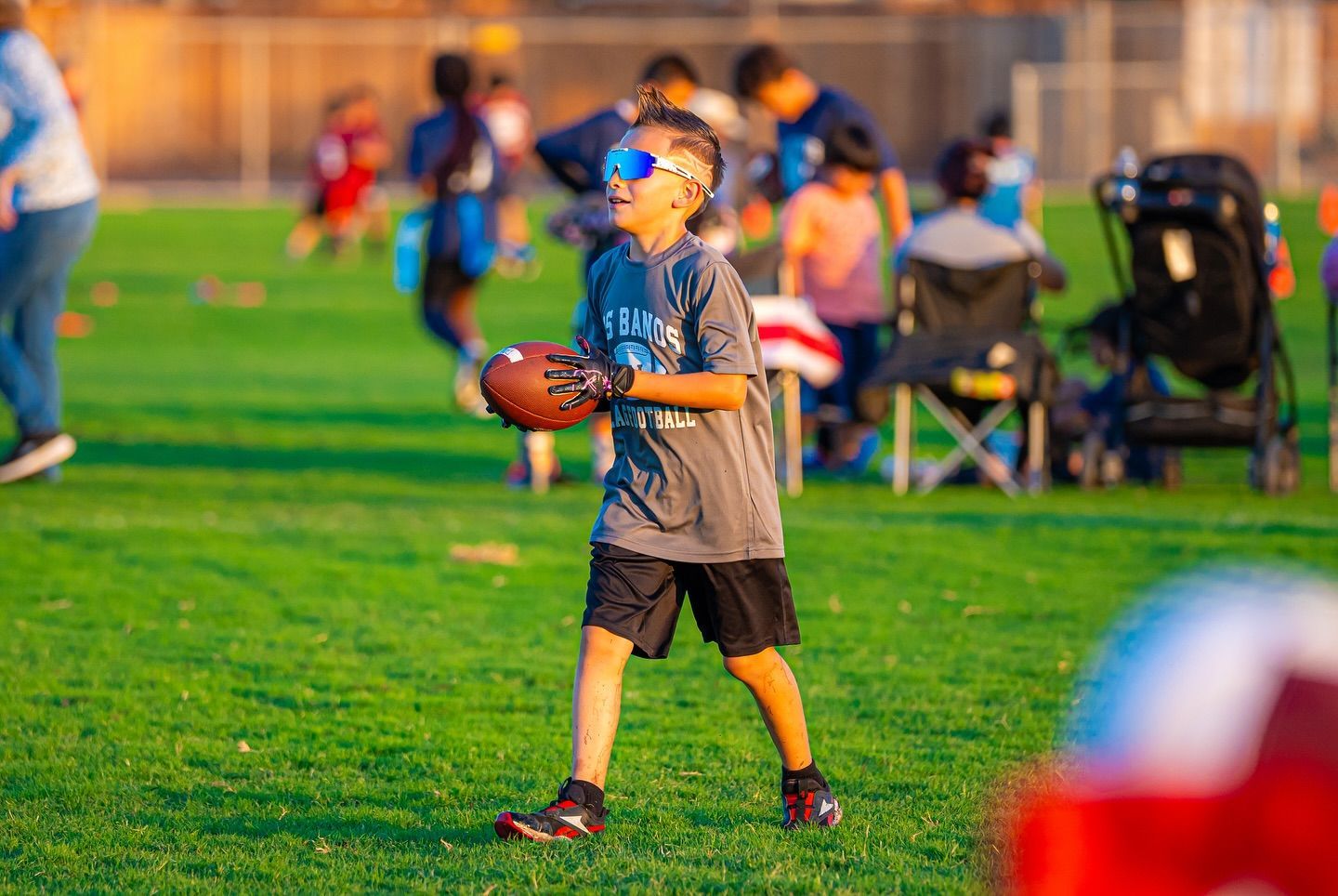 Two smiling boys with arms around each other in a park. One wears a track shirt, the other a striped shirt.