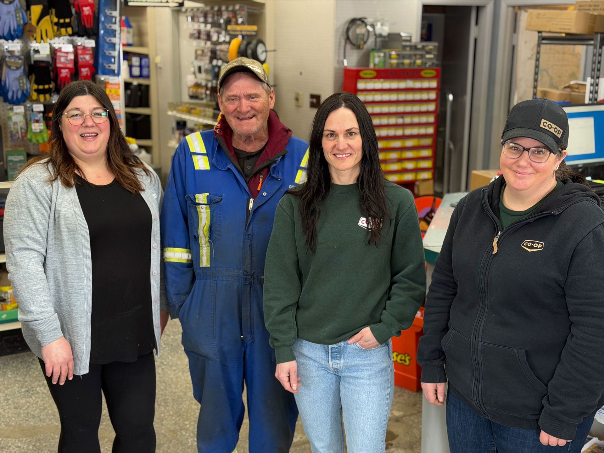 Four individuals pose together in a convenience store, with three standing and one kneeling in front.