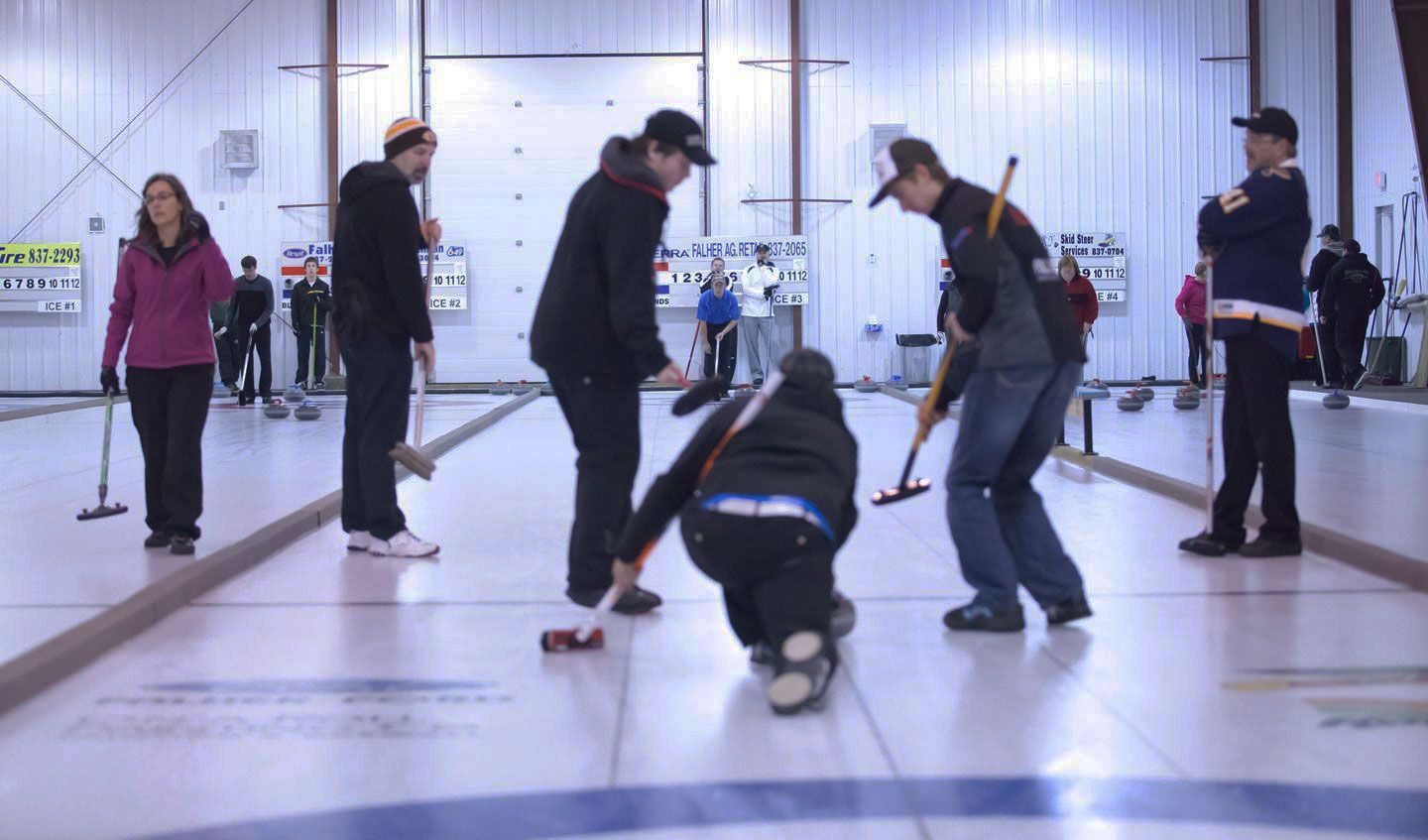 A tan and dark-brown one-story building with blue accents, two flagpoles, and a lawn under a cloudy sky.
