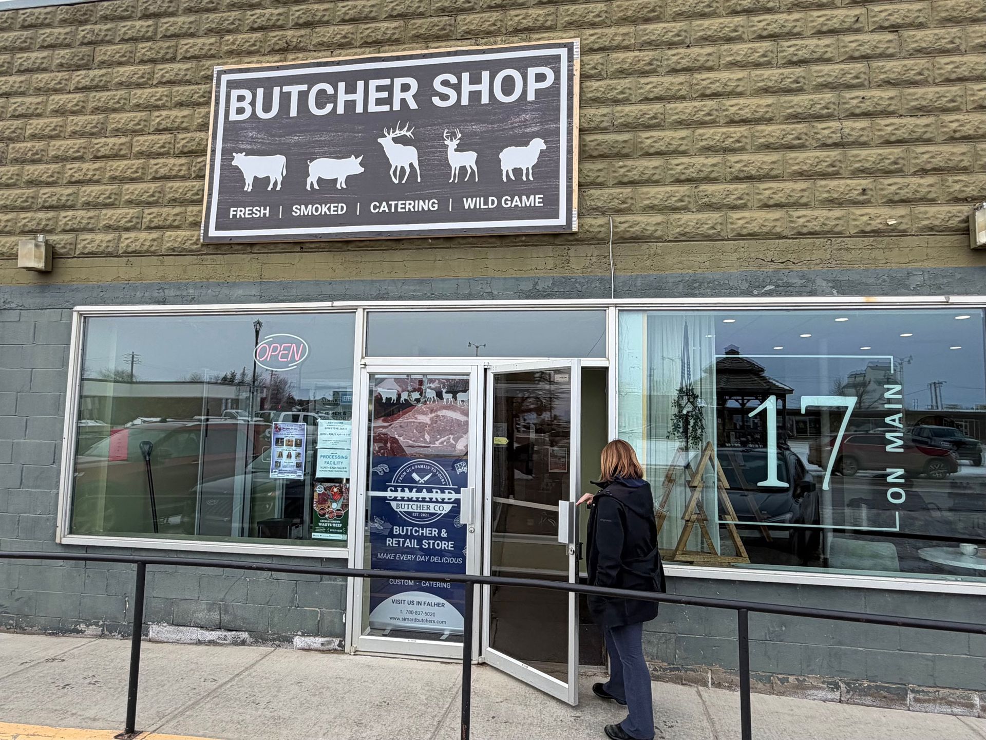 A person walks into a butcher shop on Main Street with icons of animals and text on the sign above the entrance.