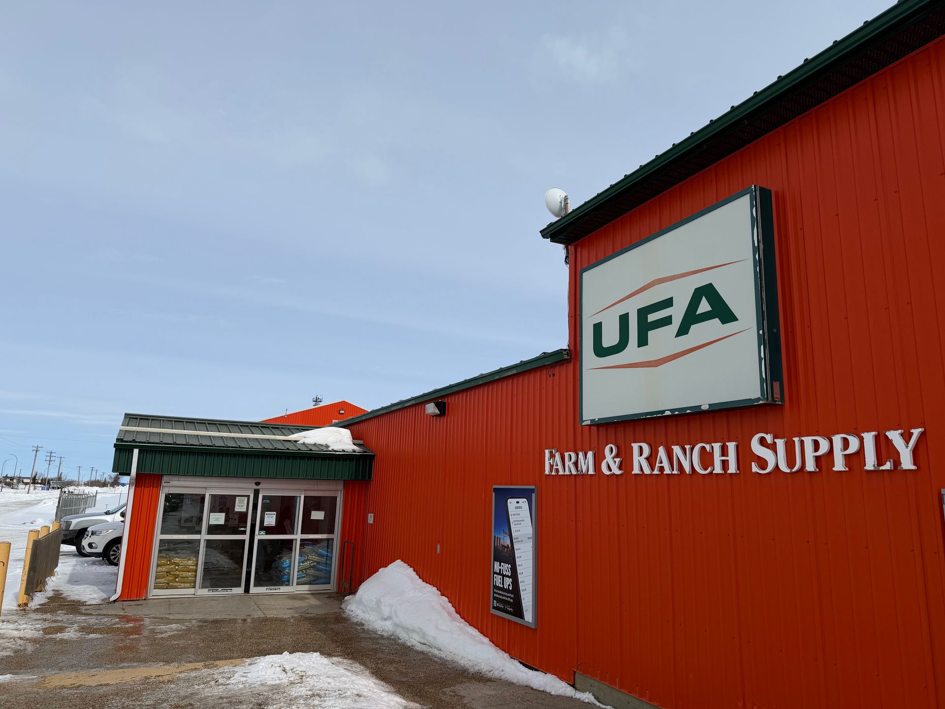 The exterior of a red UFA Farm & Ranch Supply store building with a white entrance and snow on the ground.