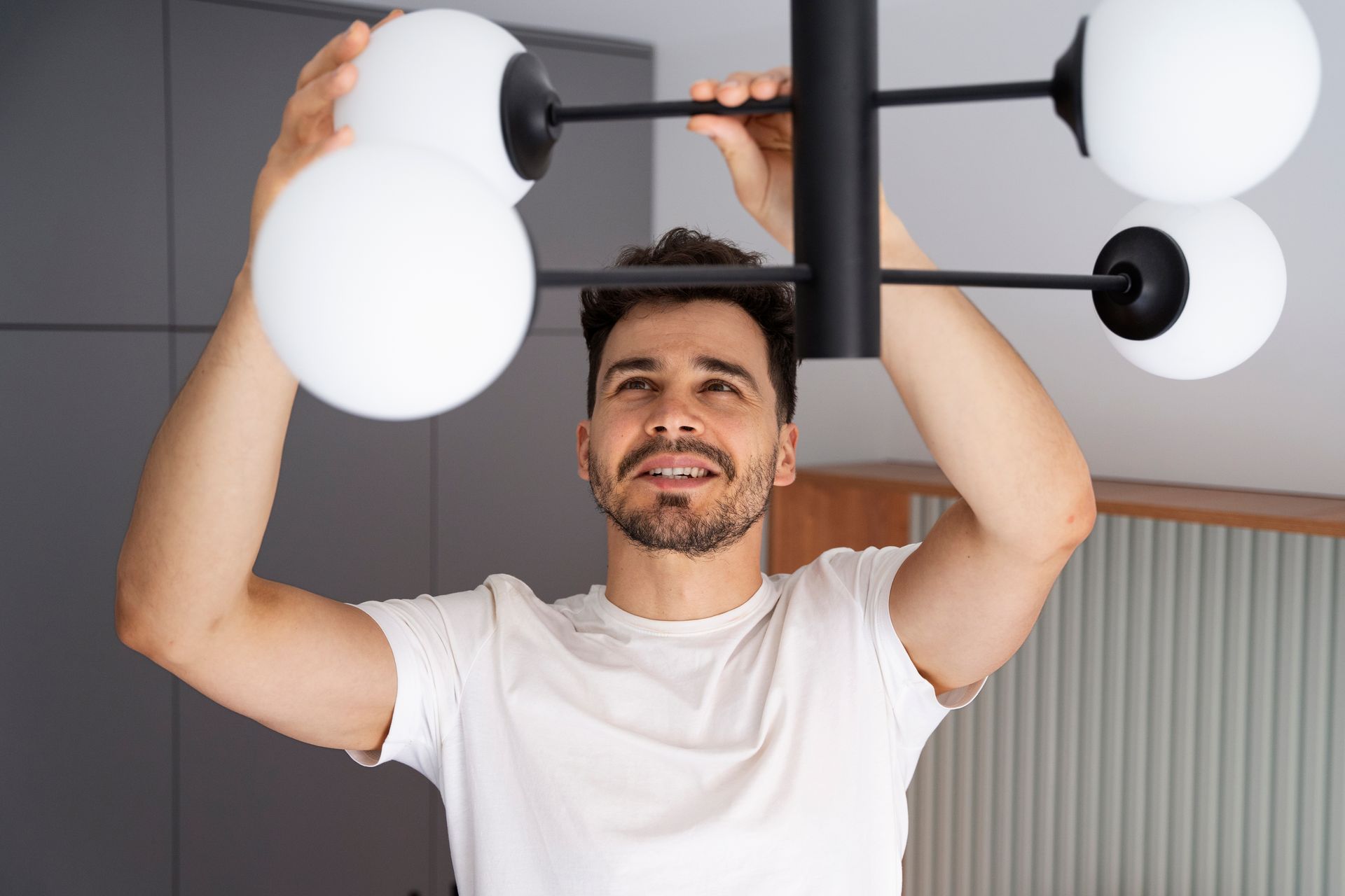 Man installing a black and white light fixture. Indoor setting, wearing a white shirt, focused expression.
