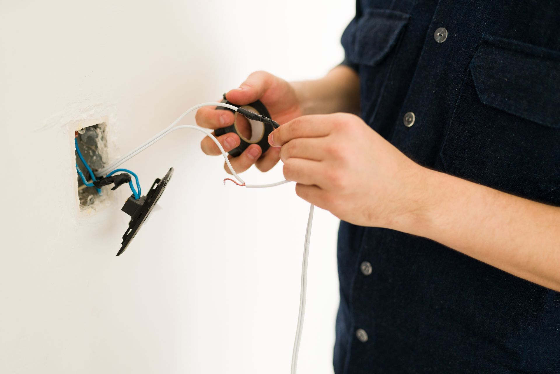Electrician wiring outlet, white wall, blue and black wires visible.
