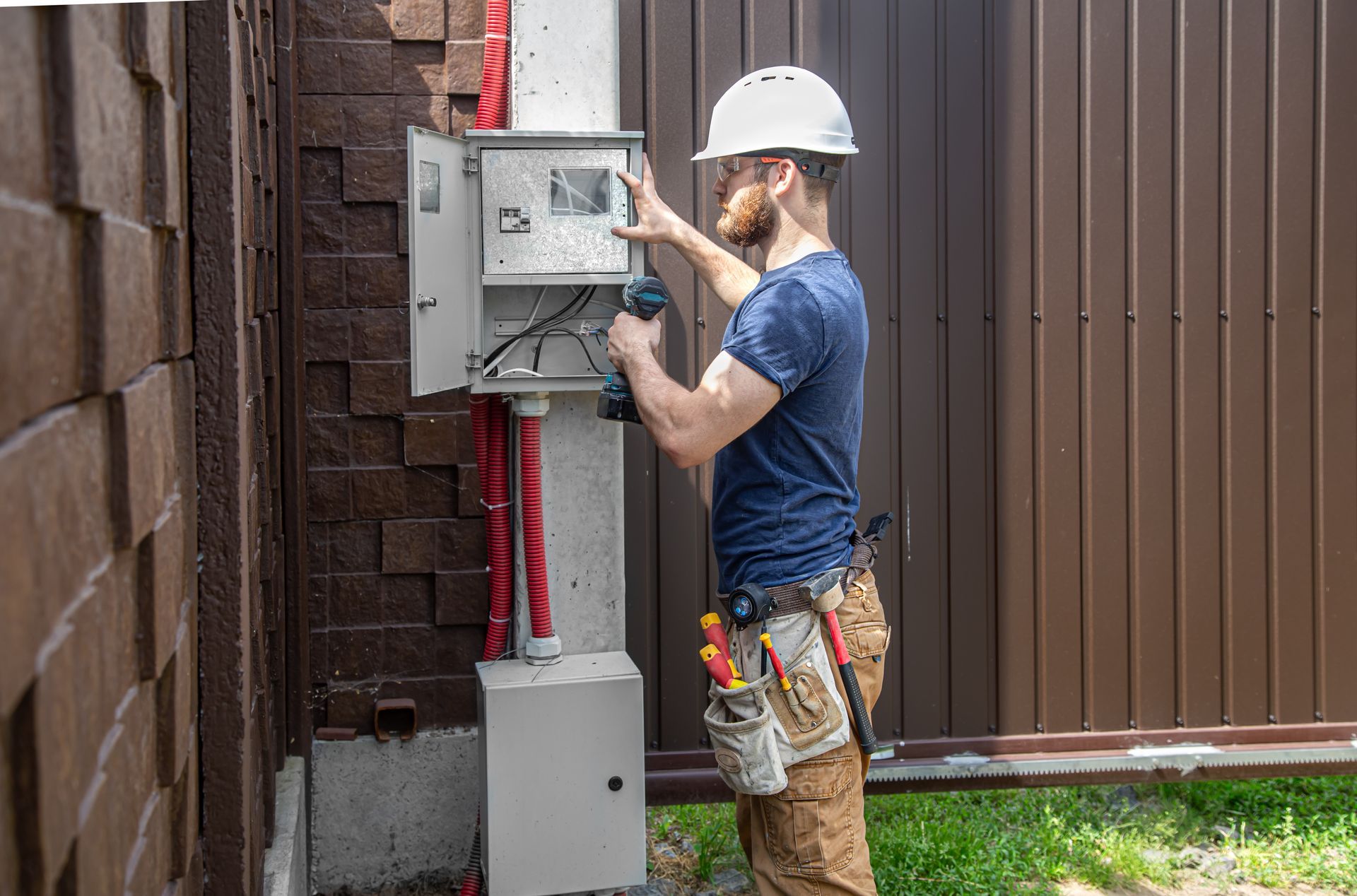 Electrician working on electrical panel outdoors next to a fence.