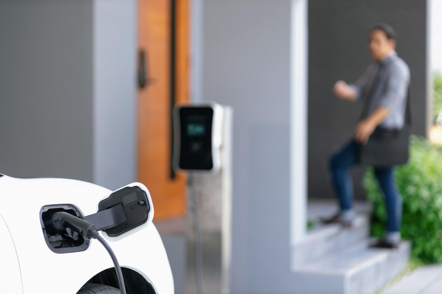 Electric vehicle charging in progress; person entering home.