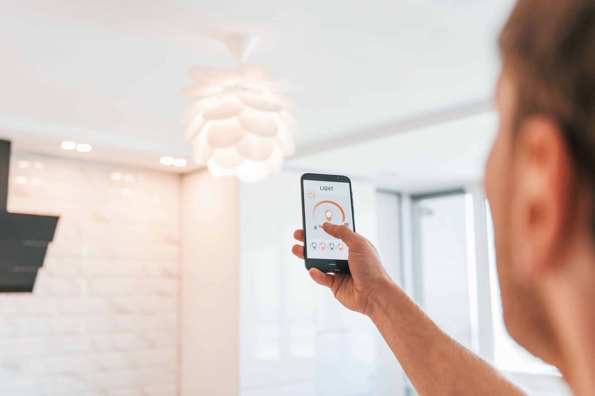 Person using smartphone to control a smart light fixture in a modern kitchen.