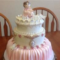 Pink and white tiered cake with a small doll topper on a wooden table