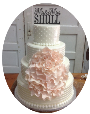 White tiered wedding cake with pearl trim, large pale pink floral decoration, and “McNeill” topper