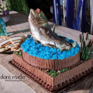 Fish-shaped cake with blue icing on a wooden table at an outdoor celebration