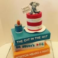 Cat in the Hat-themed layered cake with a small elephant figurine and a tiny cup on top.