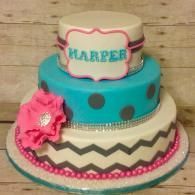 Two-tier turquoise and cream cake with pink accents and a “HARPER” topper