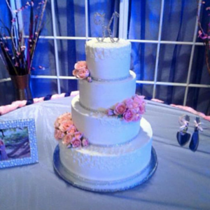 Four-tier white wedding cake with pink flowers on a decorated table