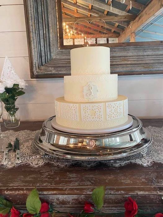 Three-tier white cake on a silver tray atop a wooden table, with a rustic mirror and flowers in the background
