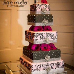 Five-tier black, white, and pink floral wedding cake with bright pink flowers on a table