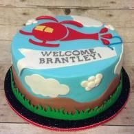 Blue birthday cake with a red helicopter and “WELCOME BRANTLEY” message on top