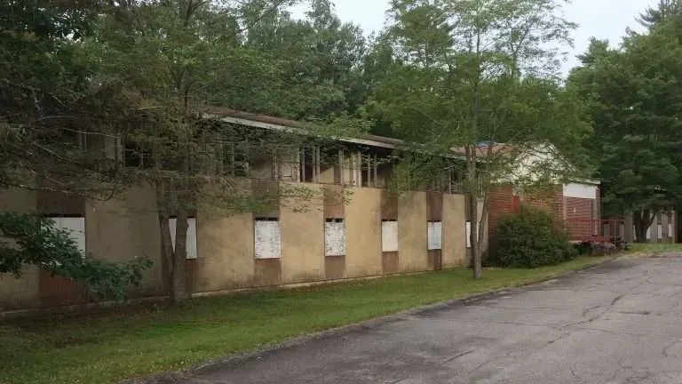 an abandoned building with a lot of windows boarded up and trees in the background .