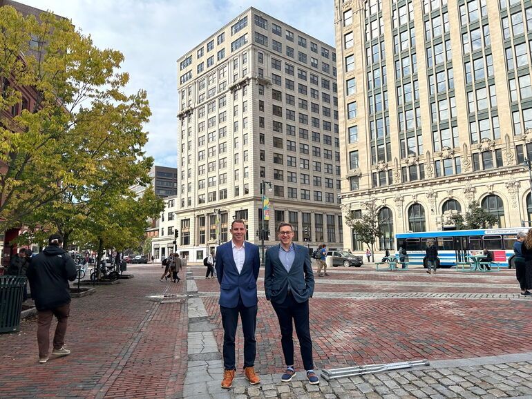two men are standing in front of a large building with a bus in the background
