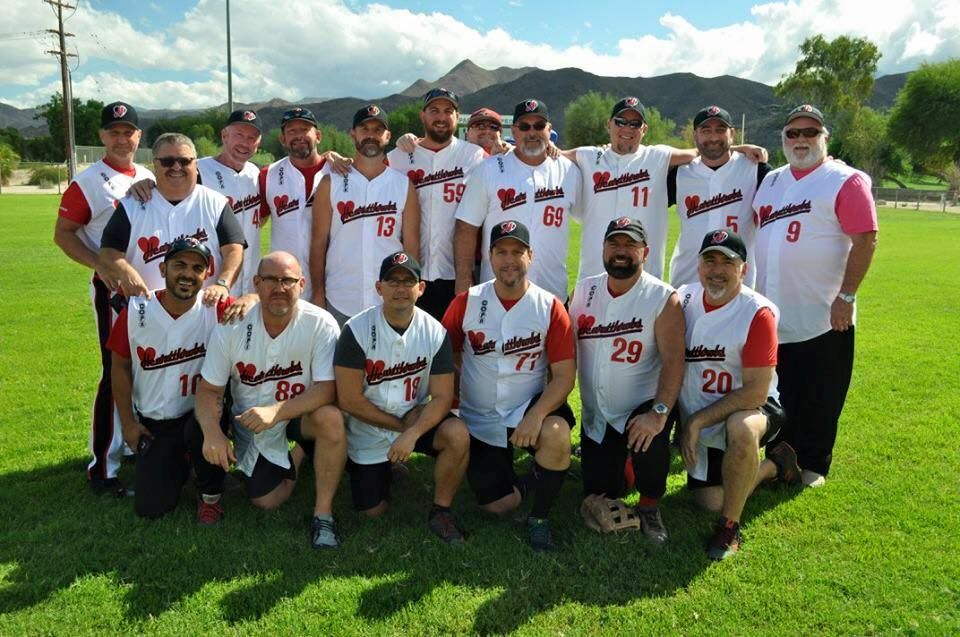 Baseball team posing on a grassy field, wearing white jerseys and caps, with mountains in the background