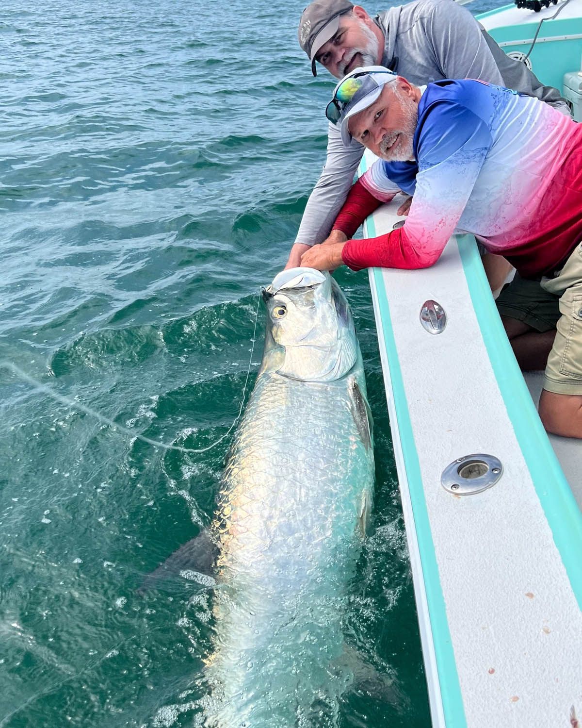 Two men are standing on a boat holding a large fish.