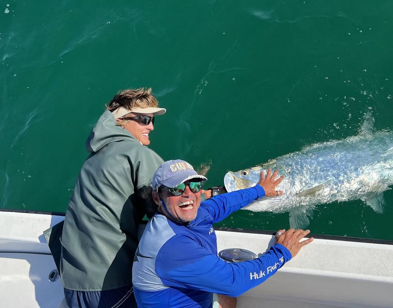 Two men are fishing on a boat and one of them is holding a fish.