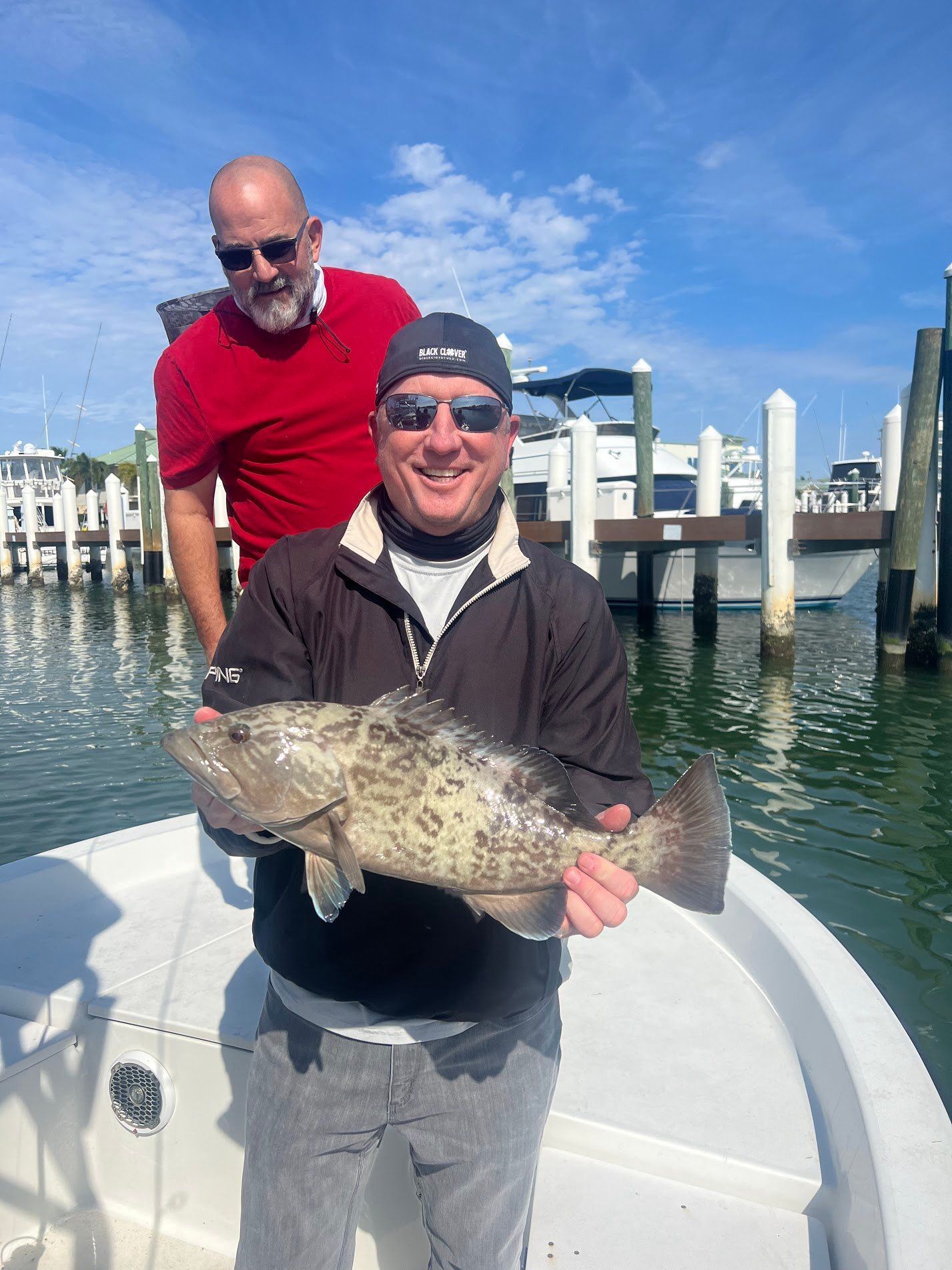 Two men are standing on a boat holding a large fish.