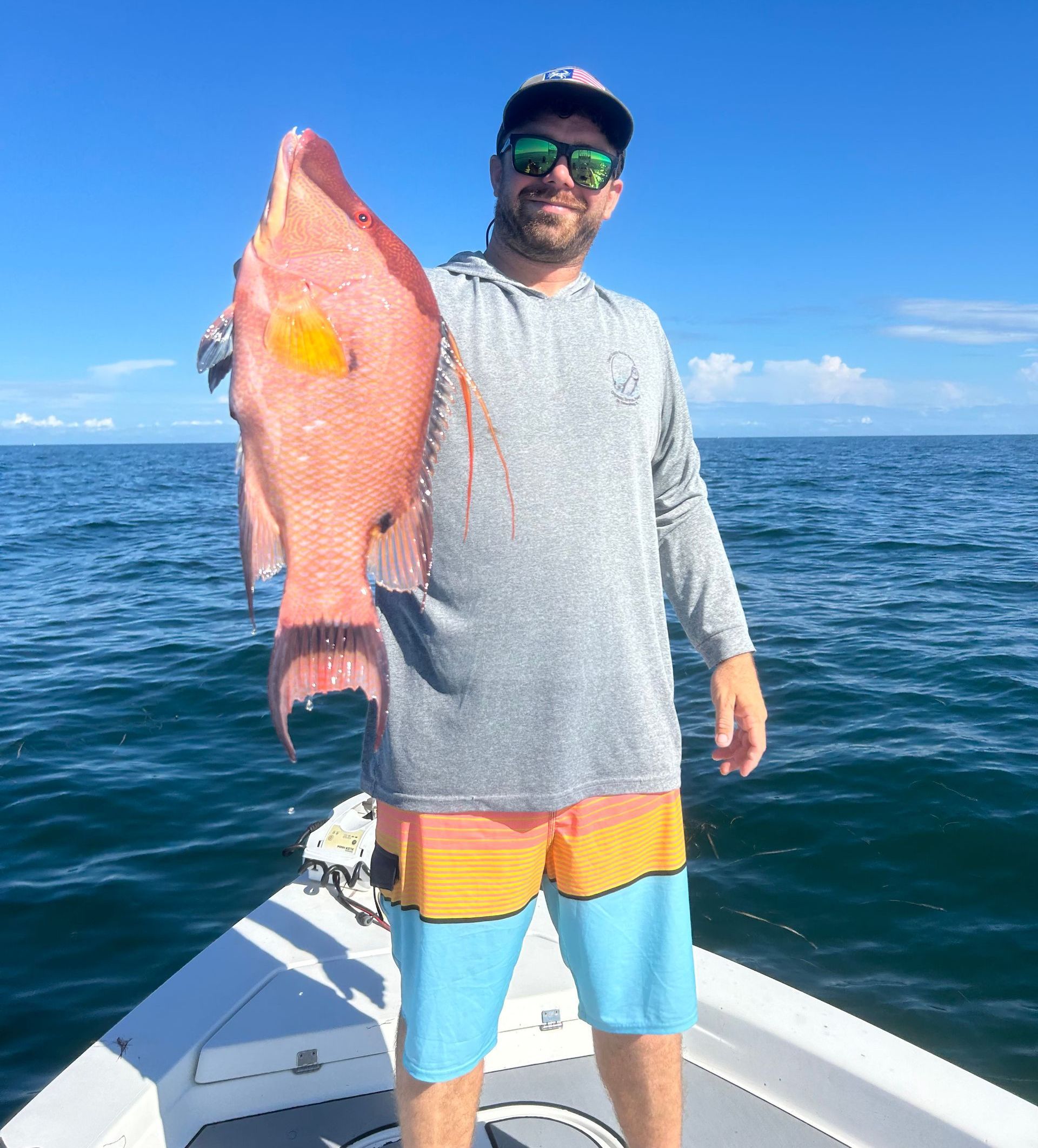 A man is standing on a boat holding a large fish.