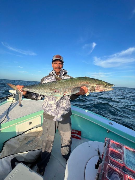 A man is holding a large fish on a boat in the ocean.