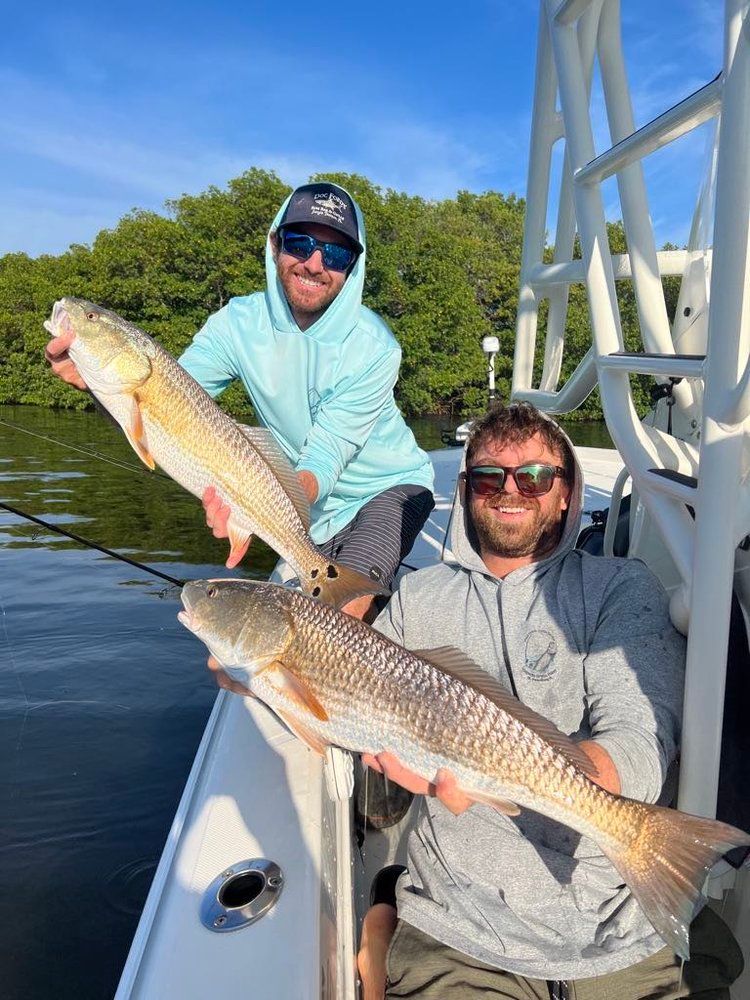 Two men are holding two redfish on a boat.