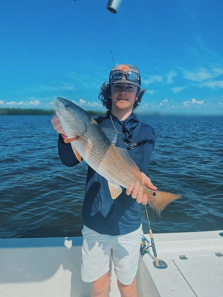 A young man is holding a large redfish on a boat.
