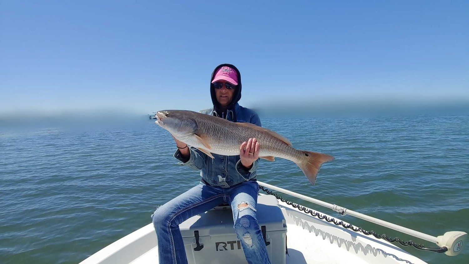 A woman is sitting on a boat holding a large fish.