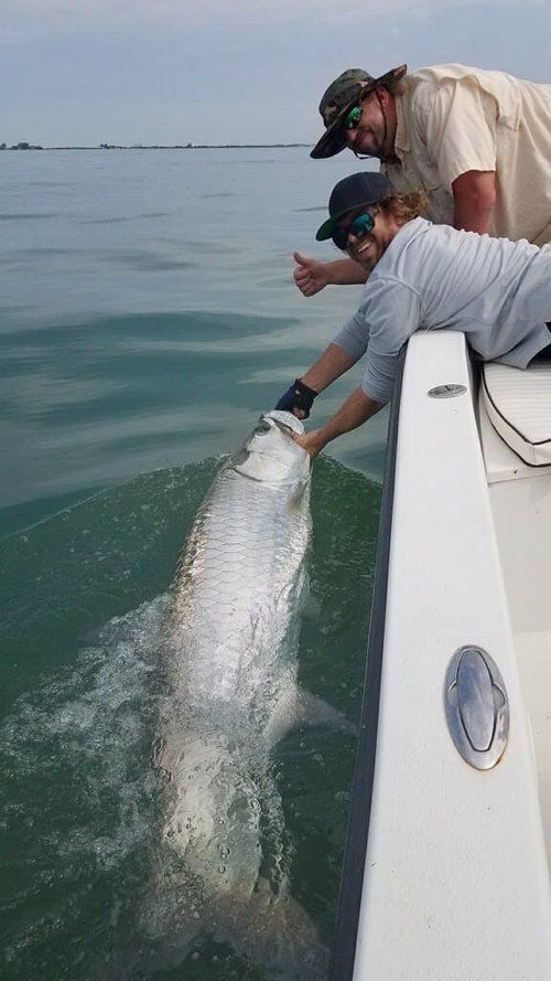 A man is holding a large fish on a boat in the water.